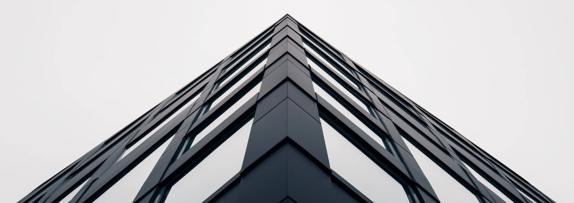 Un angle d'un bâtiment moderne vu de bas en haut, montrant une architecture en verre et en acier avec des lignes géométriques nettes, intégrant un système de Gestion Technique du Bâtiment (GTB) pour une efficacité énergétique optimale.